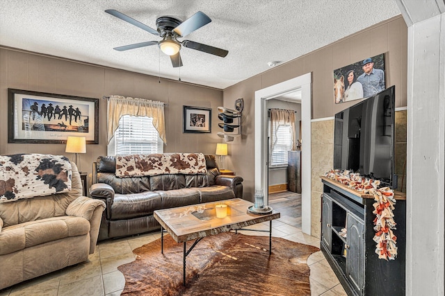 living room featuring light tile patterned floors, a textured ceiling, wooden walls, and ceiling fan