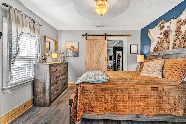 bedroom featuring multiple windows, a barn door, dark hardwood / wood-style floors, and ceiling fan