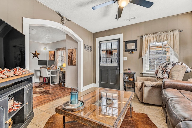 living room featuring light tile patterned flooring, wooden walls, ceiling fan, and a textured ceiling