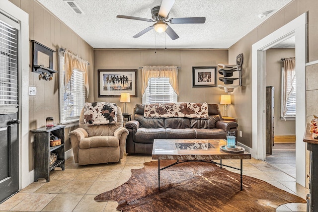 tiled living room featuring a textured ceiling, ceiling fan, and wood walls