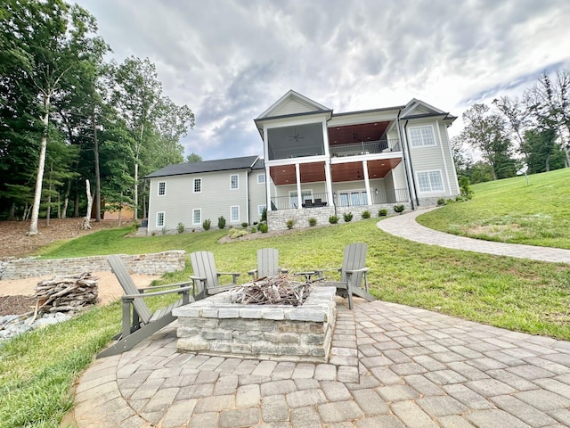 rear view of house with an outdoor fire pit, a sunroom, a lawn, and a patio