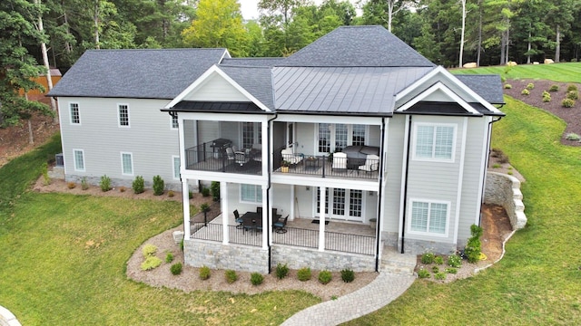 back of property with a balcony, a patio area, and a lawn
