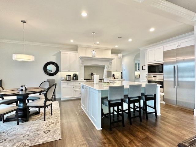 kitchen featuring white cabinets, hanging light fixtures, appliances with stainless steel finishes, and a center island with sink