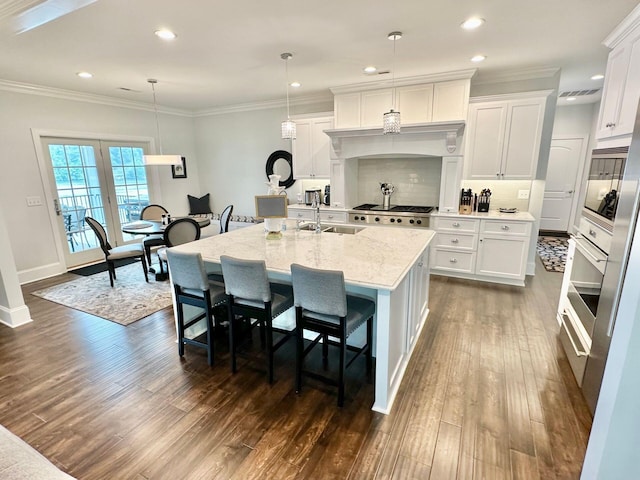 kitchen featuring a kitchen island with sink, a kitchen breakfast bar, white cabinets, decorative light fixtures, and sink