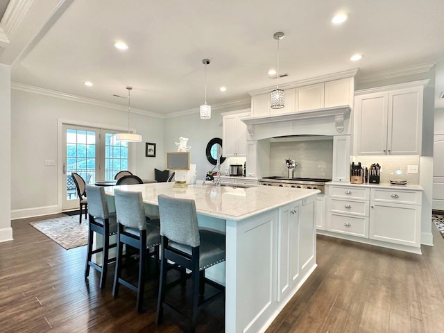 kitchen featuring white cabinetry, hanging light fixtures, a kitchen island with sink, dark hardwood / wood-style flooring, and light stone counters