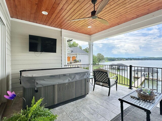 view of patio with a water view, a hot tub, and ceiling fan