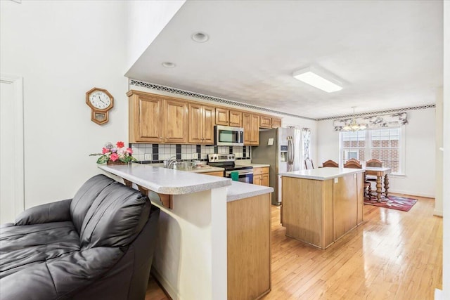 kitchen with kitchen peninsula, appliances with stainless steel finishes, decorative light fixtures, tasteful backsplash, and a kitchen bar