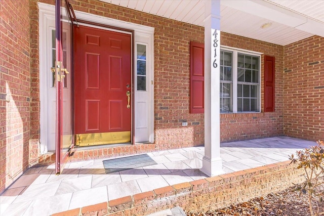 view of exterior entry with a porch and brick siding