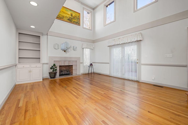 unfurnished living room featuring built in features, a towering ceiling, light hardwood / wood-style floors, and a fireplace