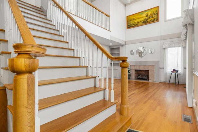 stairway featuring a towering ceiling, a tiled fireplace, and hardwood / wood-style flooring