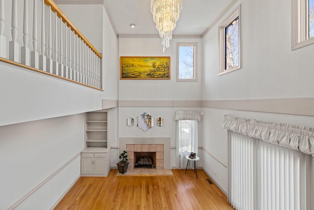 unfurnished living room featuring crown molding, a tile fireplace, light hardwood / wood-style flooring, and a notable chandelier