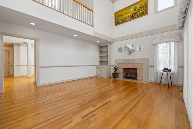 unfurnished living room with built in features, a towering ceiling, light hardwood / wood-style flooring, and a tile fireplace