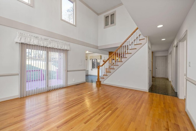 unfurnished living room with light wood-type flooring, a towering ceiling, and ornamental molding