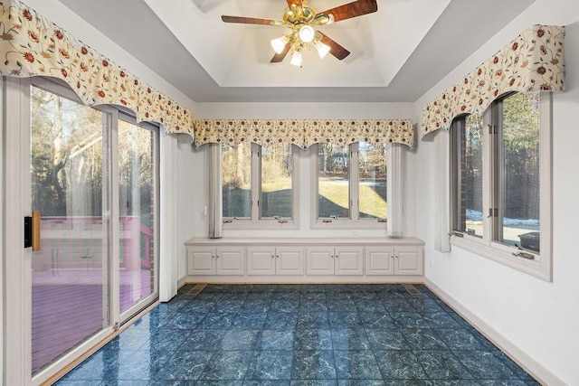 unfurnished sunroom with ceiling fan, a healthy amount of sunlight, and a tray ceiling