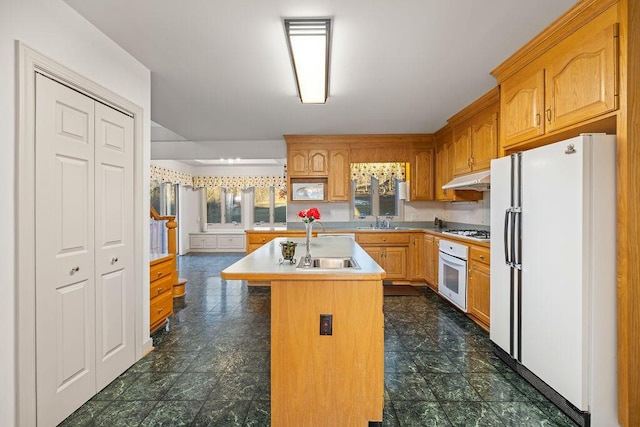 kitchen featuring sink, an island with sink, white appliances, and a breakfast bar area