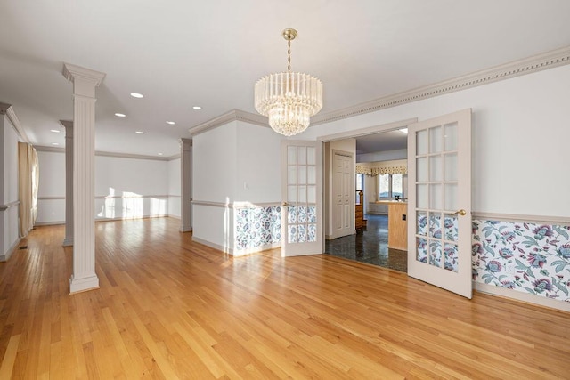 spare room with a chandelier, ornate columns, french doors, and light wood-type flooring