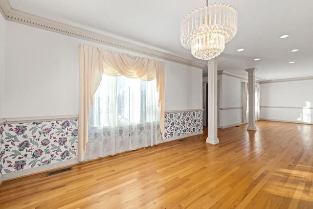 spare room with a chandelier, decorative columns, light hardwood / wood-style flooring, and ornamental molding