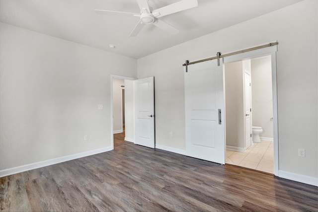 unfurnished bedroom with a barn door, wood finished floors, connected bathroom, and baseboards