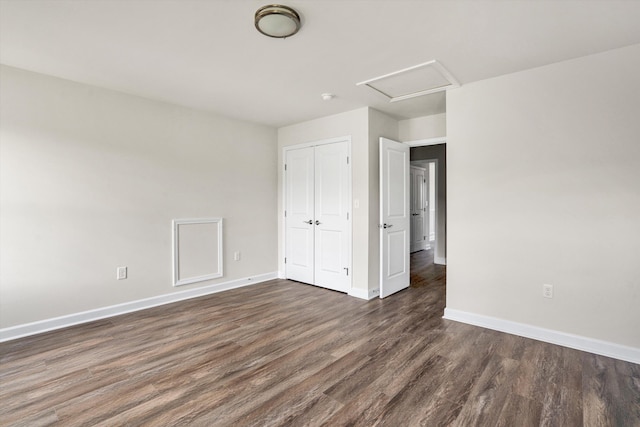 unfurnished bedroom featuring dark wood-style flooring, baseboards, a closet, and attic access