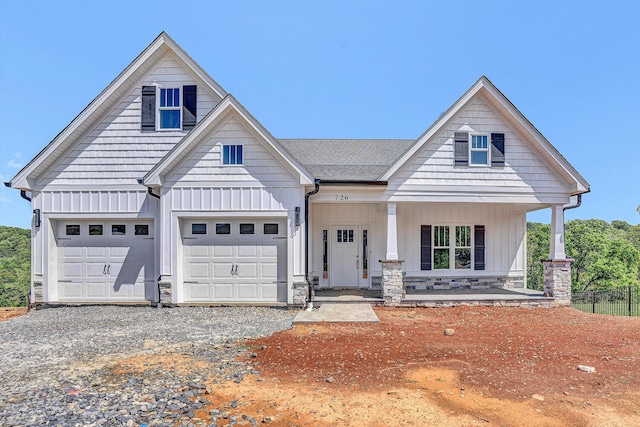 view of front of house featuring board and batten siding, gravel driveway, covered porch, stone siding, and a garage