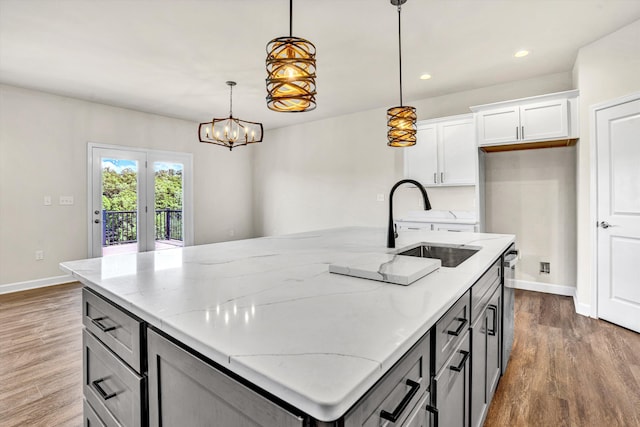 kitchen featuring baseboards, a sink, wood finished floors, an island with sink, and light stone countertops