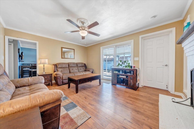 living room with a brick fireplace, crown molding, ceiling fan, and light wood-type flooring