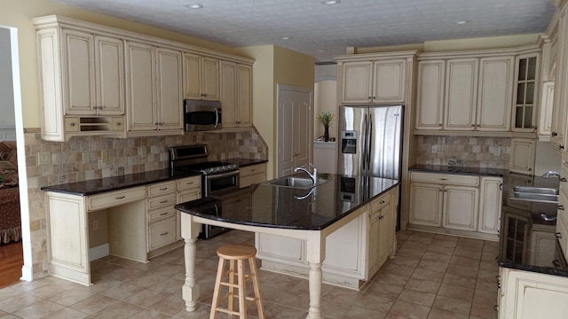 kitchen with a breakfast bar area, cream cabinets, a kitchen island with sink, a sink, and appliances with stainless steel finishes