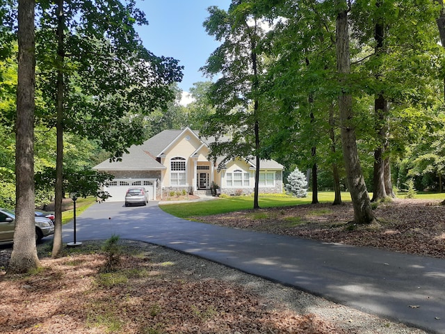 view of front of property featuring a garage, a front yard, stone siding, and driveway