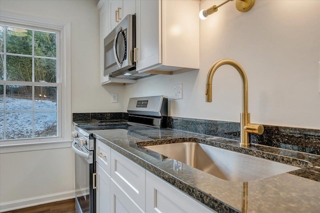 kitchen with appliances with stainless steel finishes, white cabinetry, sink, dark stone countertops, and dark hardwood / wood-style flooring