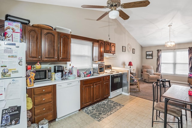 kitchen with lofted ceiling, sink, hanging light fixtures, white appliances, and ceiling fan with notable chandelier