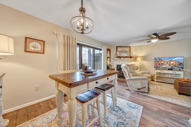 dining space with ceiling fan with notable chandelier, a tiled fireplace, and hardwood / wood-style floors