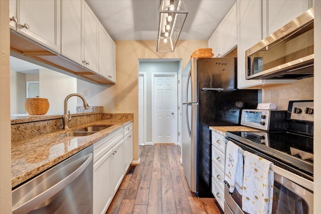 kitchen with appliances with stainless steel finishes, sink, white cabinets, and decorative light fixtures