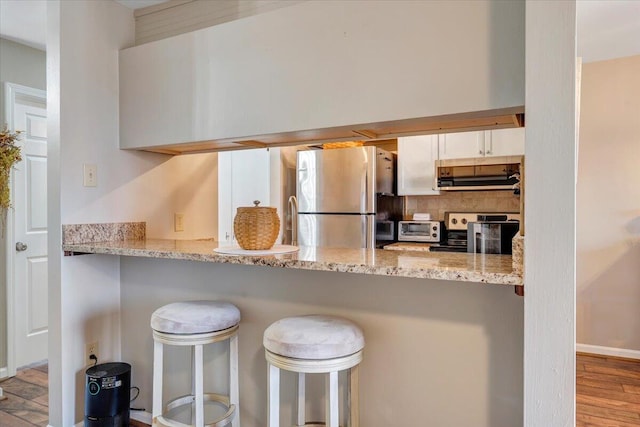 kitchen with extractor fan, white cabinets, a kitchen bar, stainless steel appliances, and light stone countertops