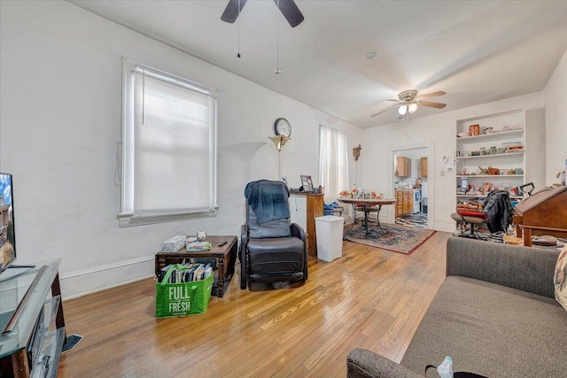 living room with built in shelves, ceiling fan, and hardwood / wood-style flooring