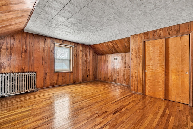 additional living space featuring hardwood / wood-style flooring, radiator heating unit, vaulted ceiling, and wood walls