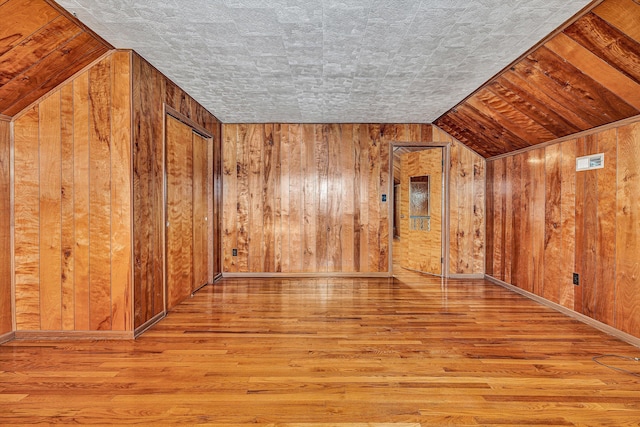 additional living space with lofted ceiling, light hardwood / wood-style floors, and wood walls