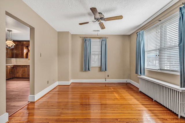 empty room featuring ceiling fan, radiator heating unit, a textured ceiling, and light hardwood / wood-style floors