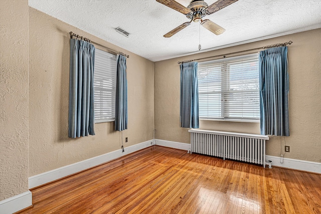 unfurnished room with radiator, hardwood / wood-style flooring, a textured ceiling, and ceiling fan