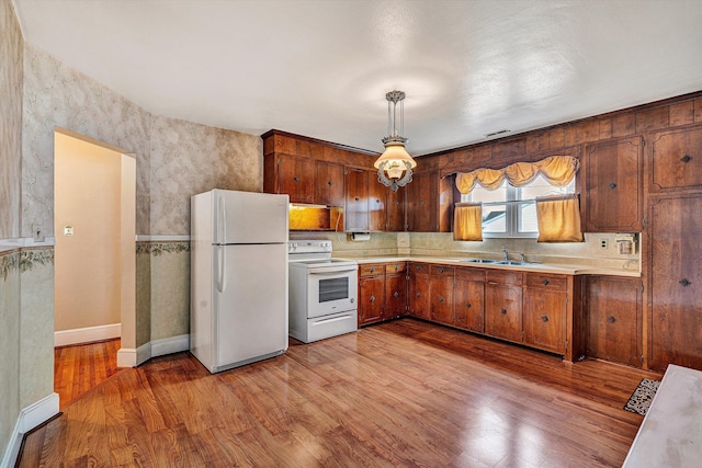 kitchen with hanging light fixtures, tasteful backsplash, white appliances, and light hardwood / wood-style floors