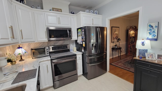 kitchen featuring appliances with stainless steel finishes, tasteful backsplash, white cabinetry, light tile patterned floors, and crown molding