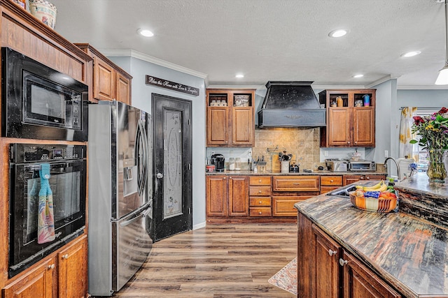 kitchen with black appliances, brown cabinetry, and custom range hood