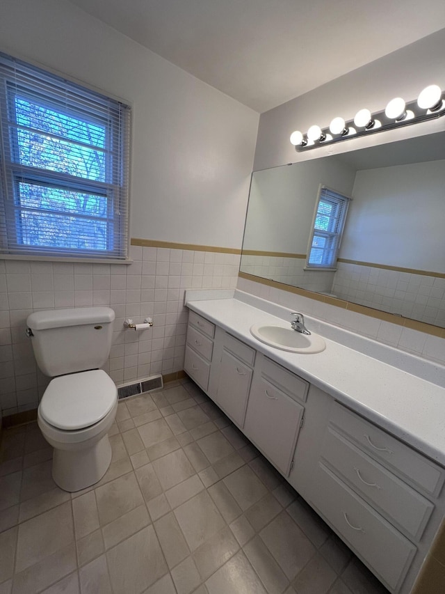 bathroom with tile walls, plenty of natural light, vanity, tile patterned floors, and toilet