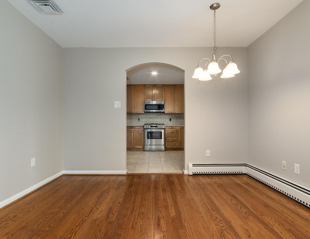 kitchen featuring light wood-type flooring, a baseboard radiator, pendant lighting, stainless steel appliances, and backsplash