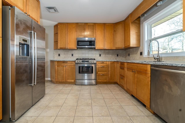 kitchen with sink, light tile patterned floors, stainless steel appliances, light stone countertops, and backsplash