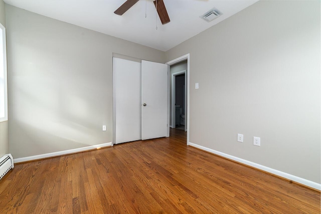 unfurnished bedroom with a baseboard heating unit, wood-type flooring, a closet, and ceiling fan