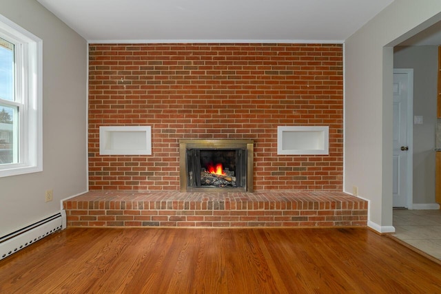 unfurnished living room featuring a baseboard radiator, wood-type flooring, and a fireplace