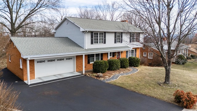 traditional-style house featuring a front yard, a shingled roof, a garage, aphalt driveway, and brick siding