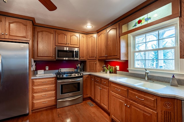 kitchen with brown cabinetry, appliances with stainless steel finishes, wood finished floors, and a sink