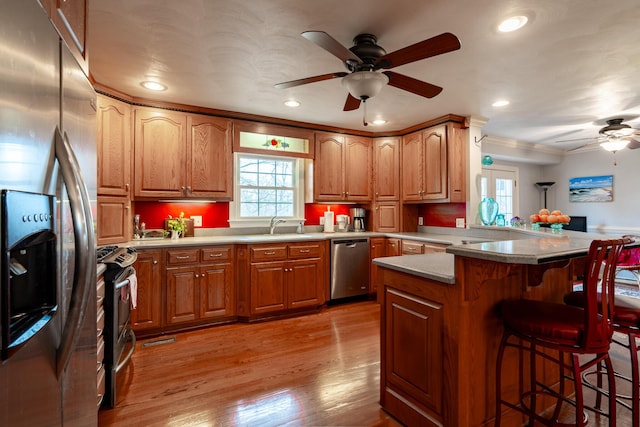 kitchen with a kitchen breakfast bar, appliances with stainless steel finishes, a peninsula, a ceiling fan, and a sink