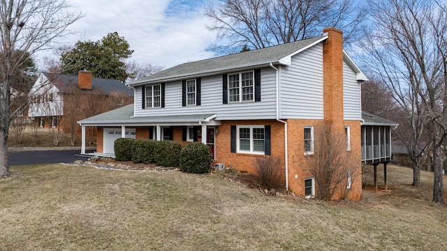 view of front of property with a front lawn, aphalt driveway, a garage, brick siding, and a chimney